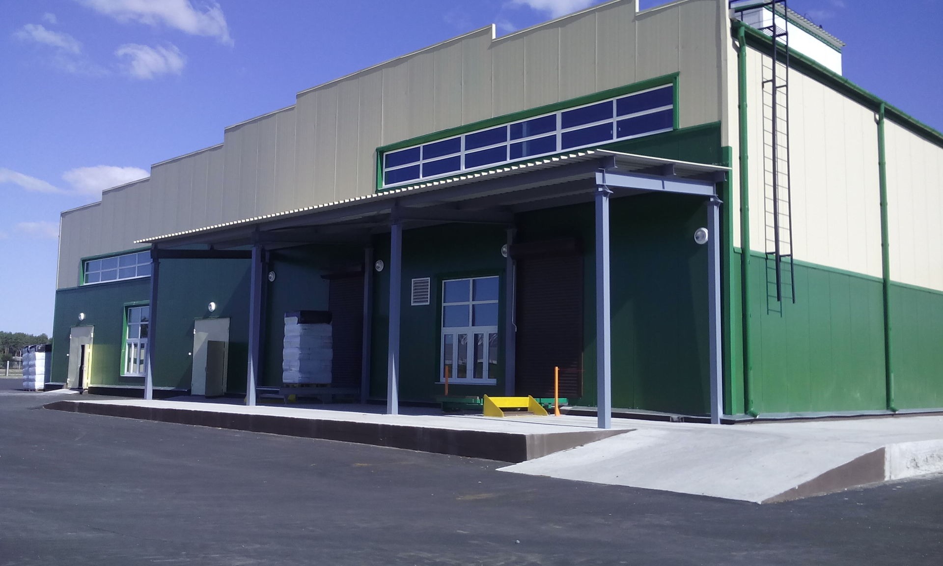 Magazyn z rampą załadunkową, zielono-białe ściany, metalowa konstrukcja zadaszenia i drabina na elewacji.
