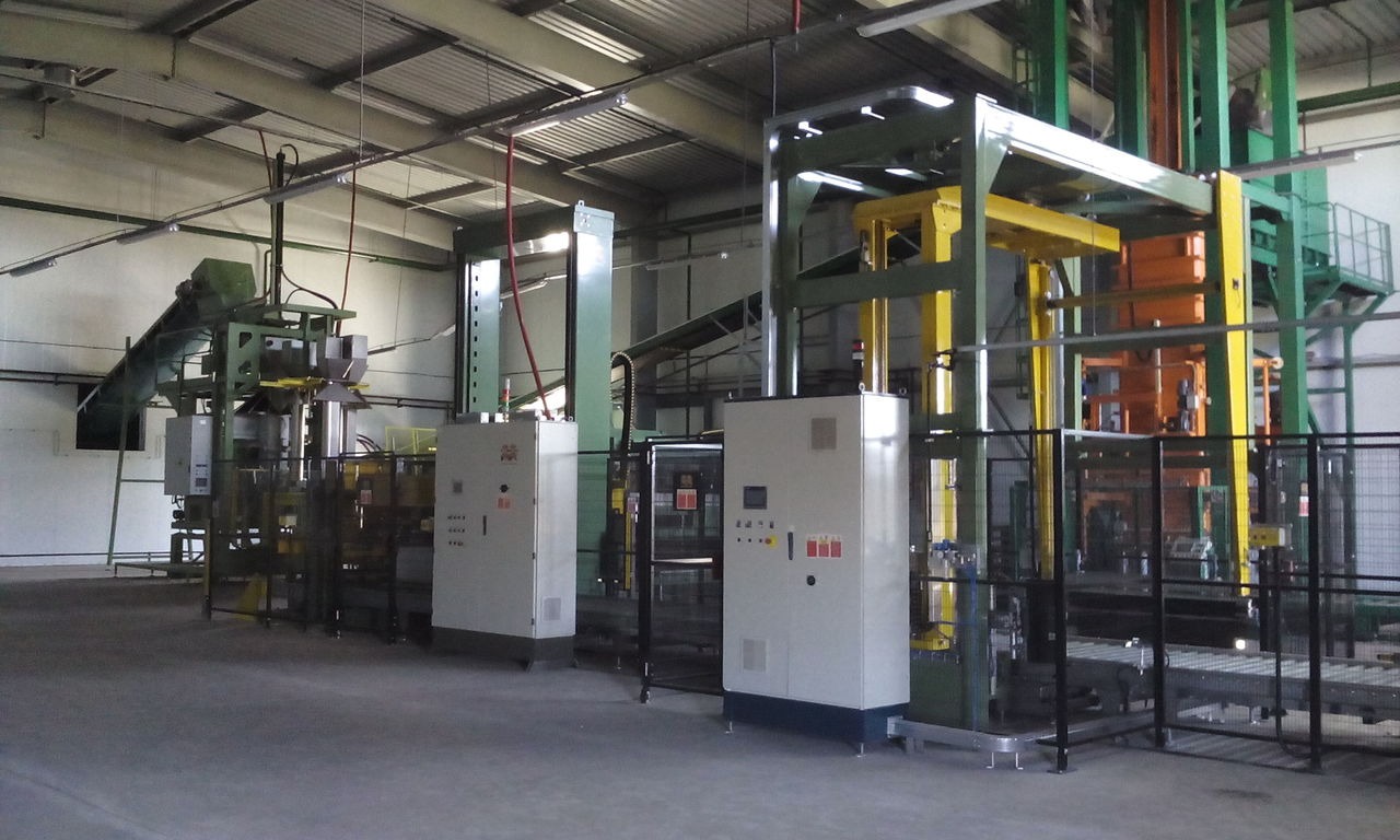 Automatyczna linia do nawozów w hali produkcyjnej, z podajnikiem taśmowym i panelami sterowania.