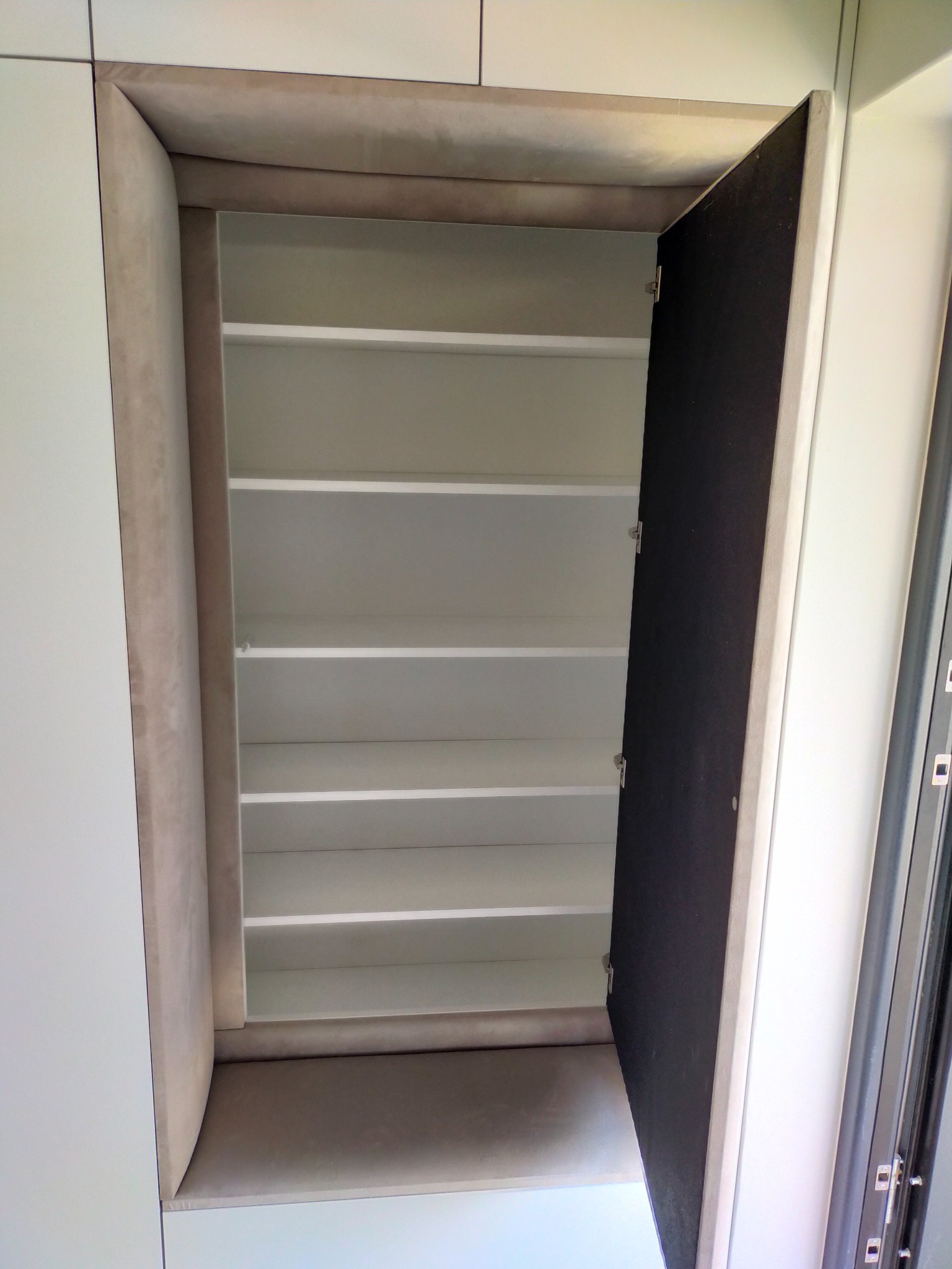 Otwarta szafa wnękowa z półkami i tapicerowanym obramowaniem w kolorze beżowym, widok z dołu.