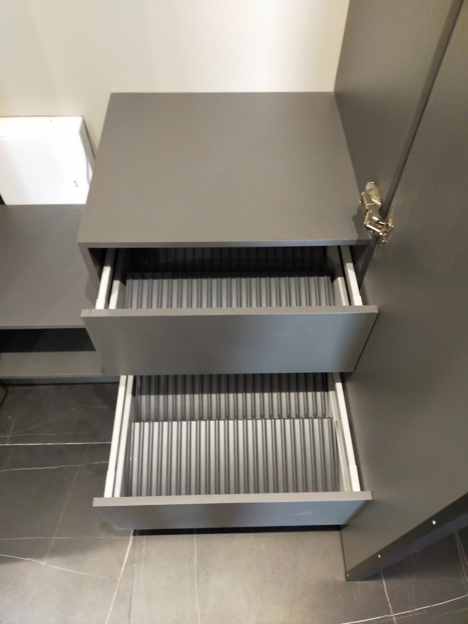 Szare szafki z wysuwanymi szufladami z pionowymi przegródkami, widoczne zawiasy na drzwiach.