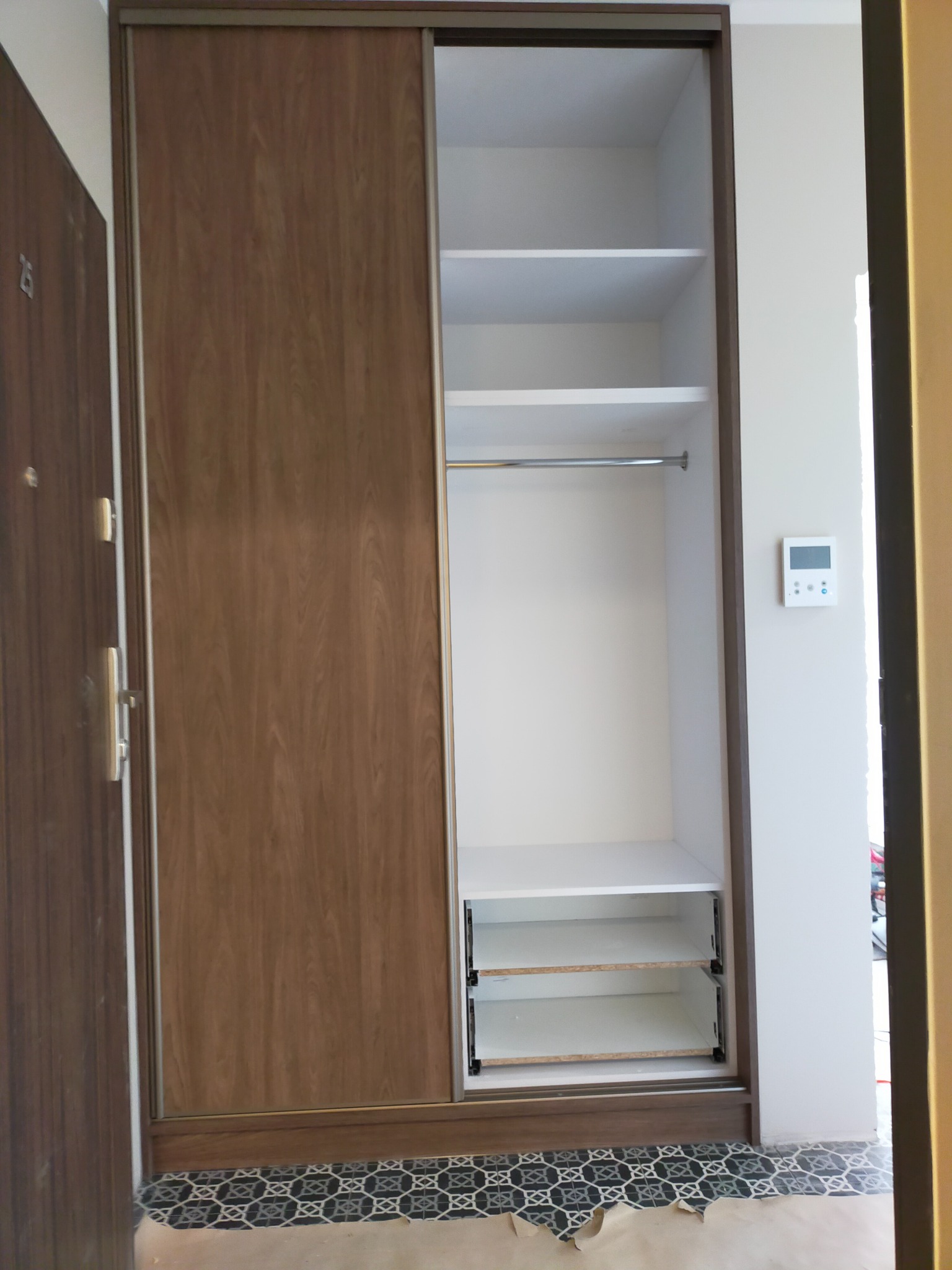 Wnętrze szafy wnękowej z przesuwnymi drzwiami o drewnopodobnym wykończeniu, widoczne półki i drążek na ubrania, podłoga zabezpieczona kartonem.