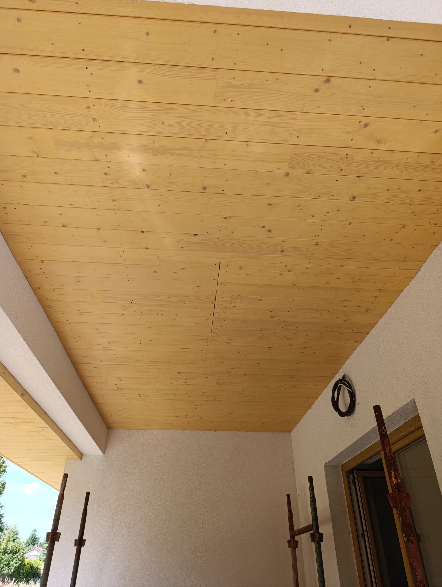 Drewniana podbitka dachowa z widocznymi sękami i usłojeniem, zamontowana na zewnątrz budynku. W tle fragment ściany i rusztowania.