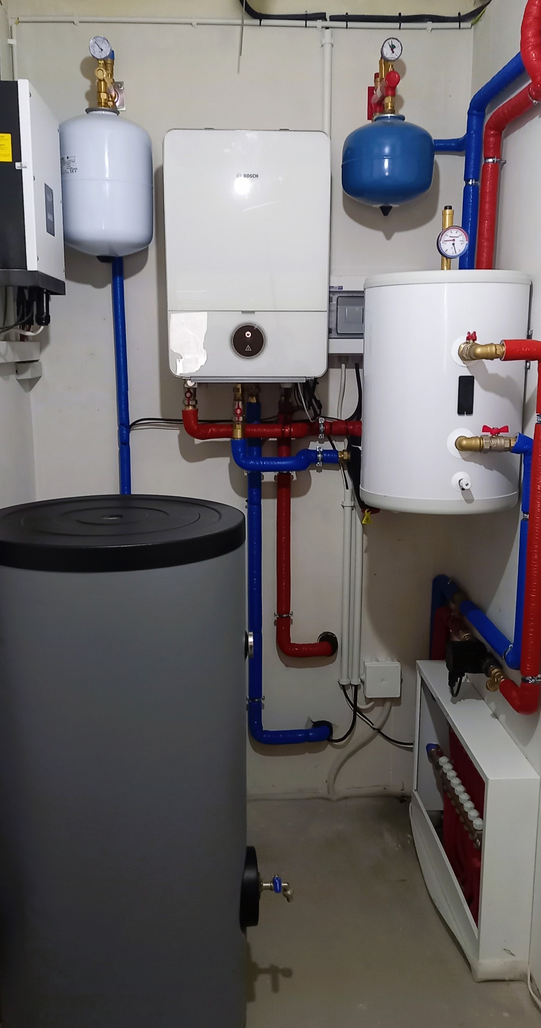 Kompletna instalacja kotła grzewczego Bosch z zasobnikami ciepłej wody i naczyniami przeponowymi, rury w kolorze czerwonym i niebieskim, manometry na górze zbiorników, widok z dołu.