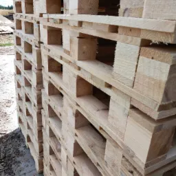 Stos jasnych, drewnianych palet ułożonych jeden na drugim, widoczne słoje drewna i konstrukcja nośna, tło rozmyte z zielenią.