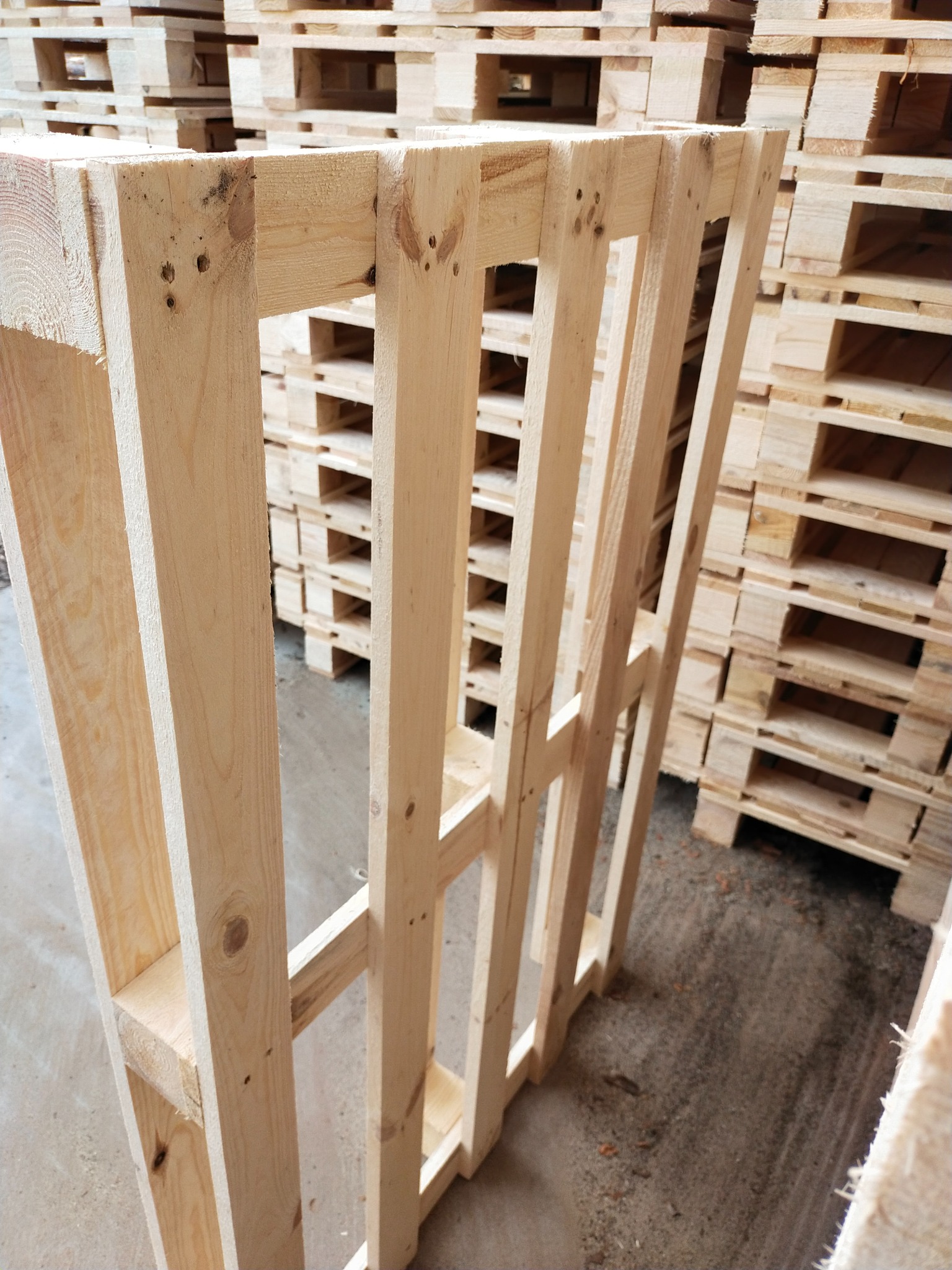 Jasne, drewniane palety ułożone w stos, widoczne ślady po gwoździach na elementach konstrukcyjnych.