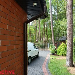 EXEACTIVE - Kamera monitoringu kopułkowa zamontowana pod okapem budynku z cegły. Widoczny samochód dostawczy i brama w tle.