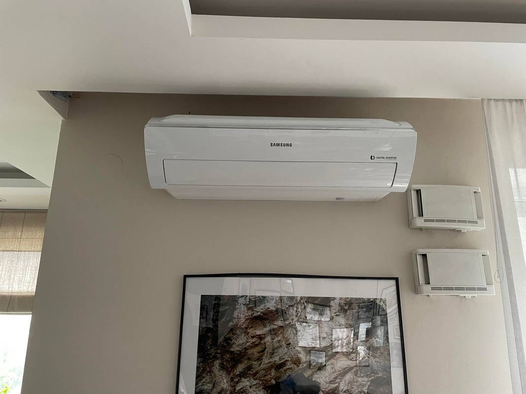 Biała jednostka wewnętrzna klimatyzacji Samsung zamontowana na beżowej ścianie w pomieszczeniu, widoczne dwa nawiewniki ścienne i obraz w czarnej ramie pod spodem.
