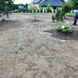 Firma Agpol - Przygotowanie terenu pod trawnik: mężczyzna grabi ziemię z siatką wzmacniającą, widoczne drzewka ozdobne, krzewy i kwiaty lawendy w tle.