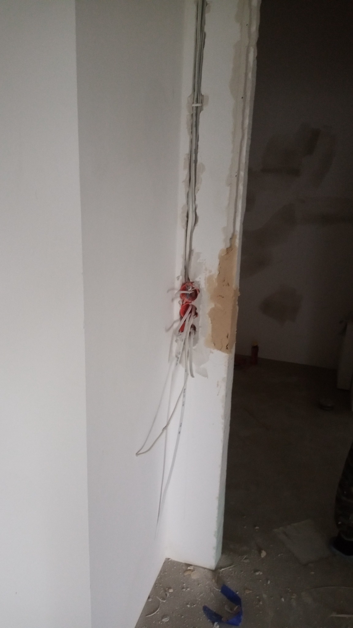 Wiązka przewodów elektrycznych wystająca ze ściany w trakcie prac instalacyjnych, widoczne puszki połączeniowe i przewody w białej izolacji, surowy stan wykończenia wnętrza.