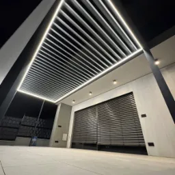 Nowoczesna pergola z żaluzjami fasadowymi, oświetleniem LED i betonową posadzką. Ujęcie z dołu podkreśla geometryczny design i minimalistyczny charakter.