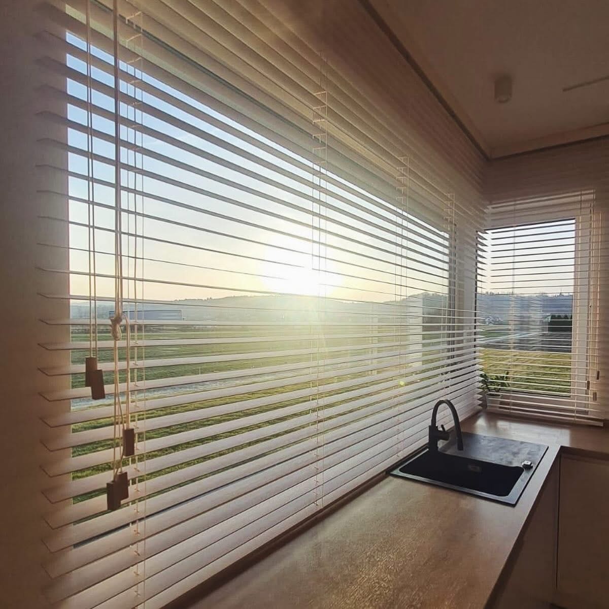 Jasne, drewniane żaluzje poziome w kuchni z widokiem na poranne słońce. Minimalistyczny design, ciepłe światło, nowoczesna armatura kuchenna.