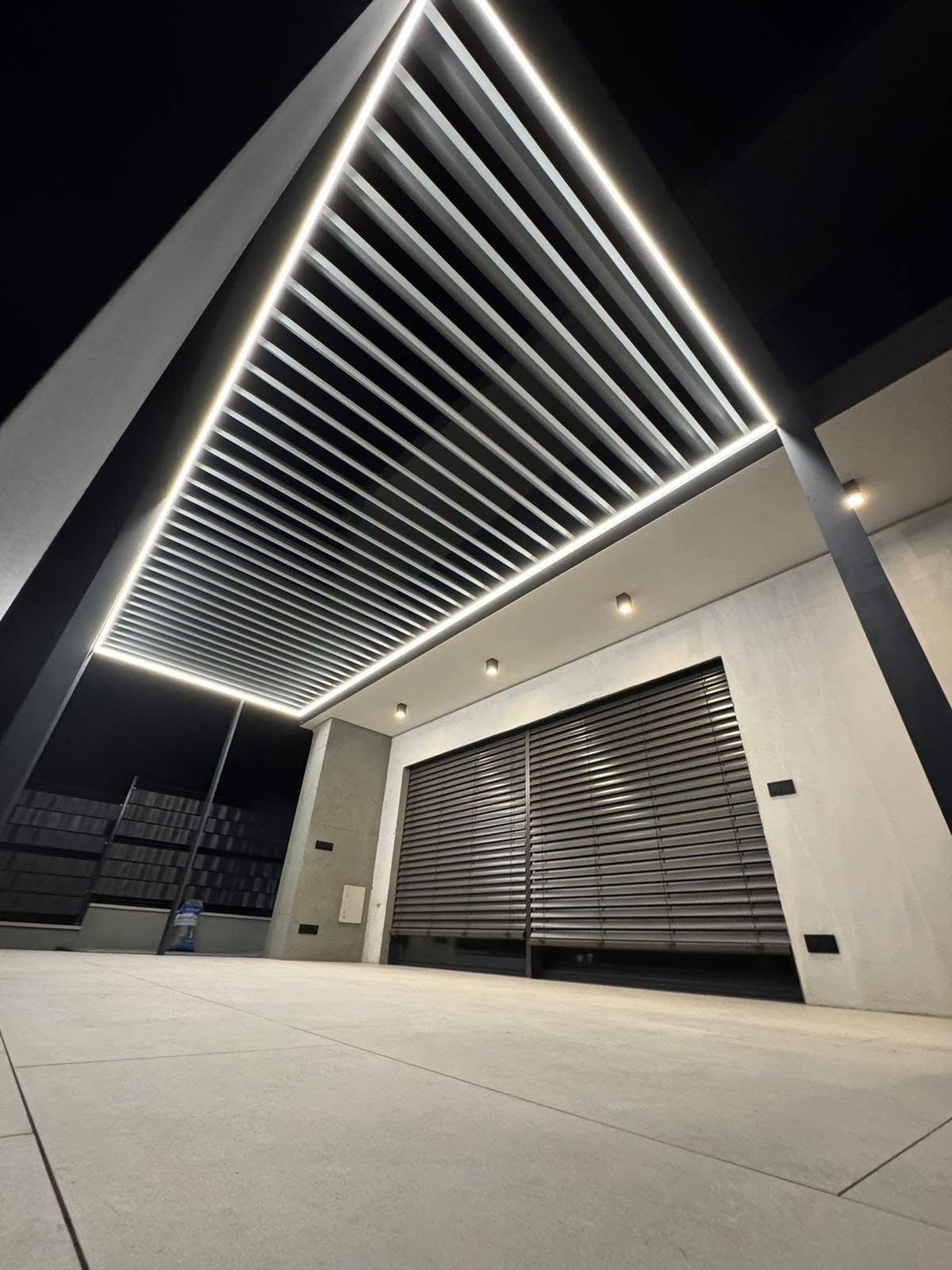 Nowoczesna pergola z żaluzjami fasadowymi, oświetleniem LED i betonową posadzką. Ujęcie z dołu podkreśla geometryczny design i minimalistyczny charakter.