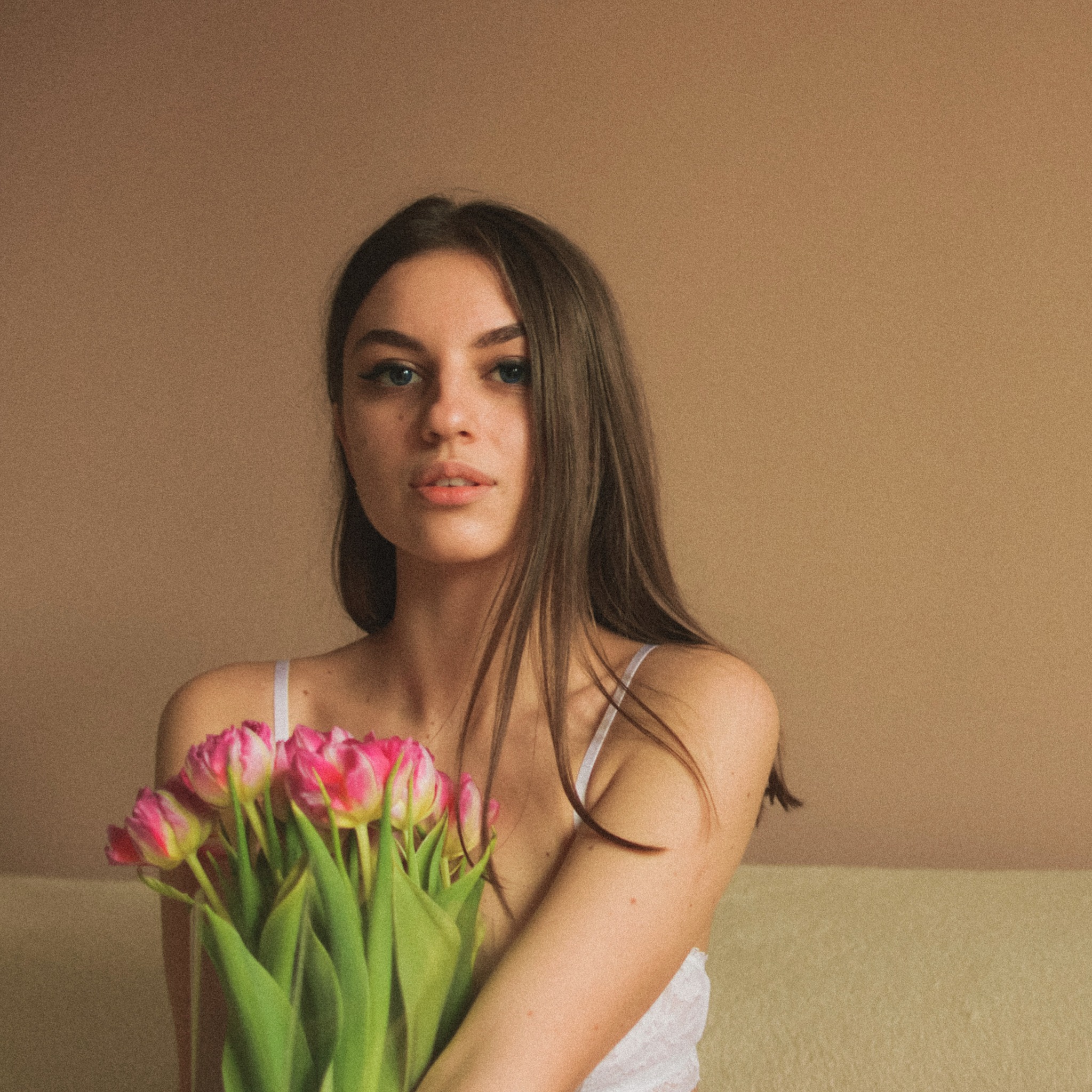 Portret młodej kobiety z bukietem różowych tulipanów na beżowym tle w Białymstoku.