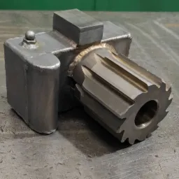 Metalowa konstrukcja z przyspawanym elementem przypominającym frez, widoczne spawy, całość na metalowym stole warsztatowym.