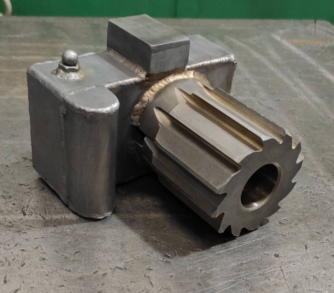 Metalowa konstrukcja z przyspawanym elementem przypominającym frez, widoczne spawy, całość na metalowym stole warsztatowym.