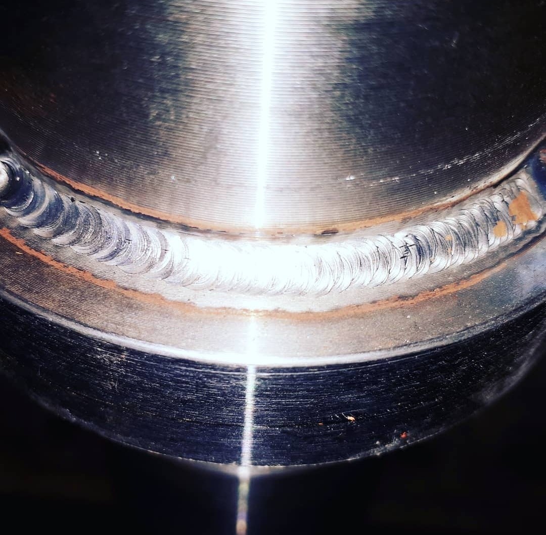 Metalowy element po procesie łączenia, widoczne regularne ślady spoiny na okrągłej powierzchni.