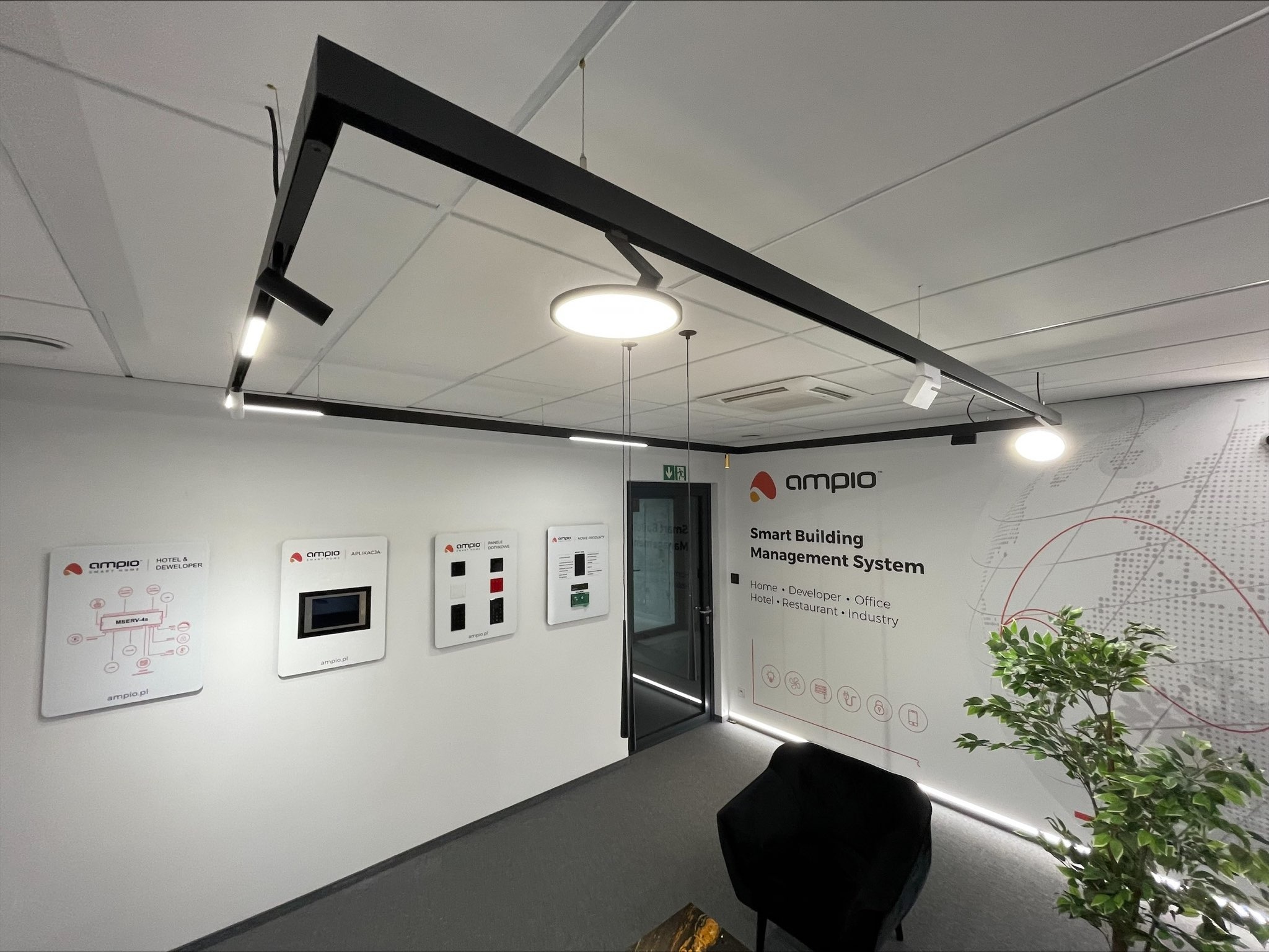 Salon z systemem inteligentnego budynku Ampio, prezentujący panele dotykowe, aplikacje i rozwiązania dla hoteli, deweloperów, biur, restauracji i przemysłu, z nowoczesnym oświetleniem szynowym...