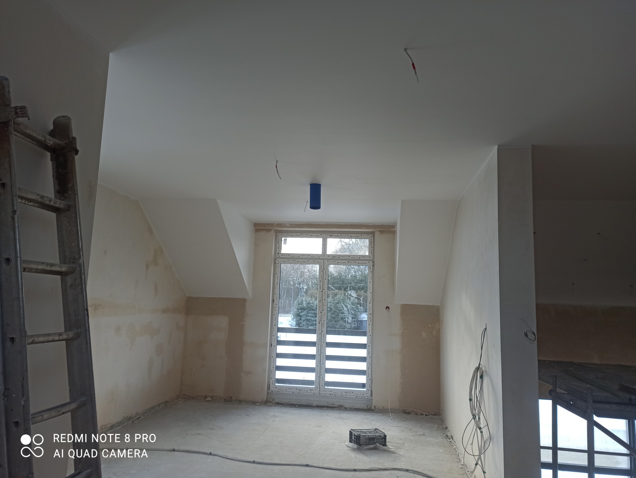 Wnętrze pokoju w trakcie prac wykończeniowych: ściany przygotowane do malowania, sufit pomalowany na biało, widoczne kable i drabina.