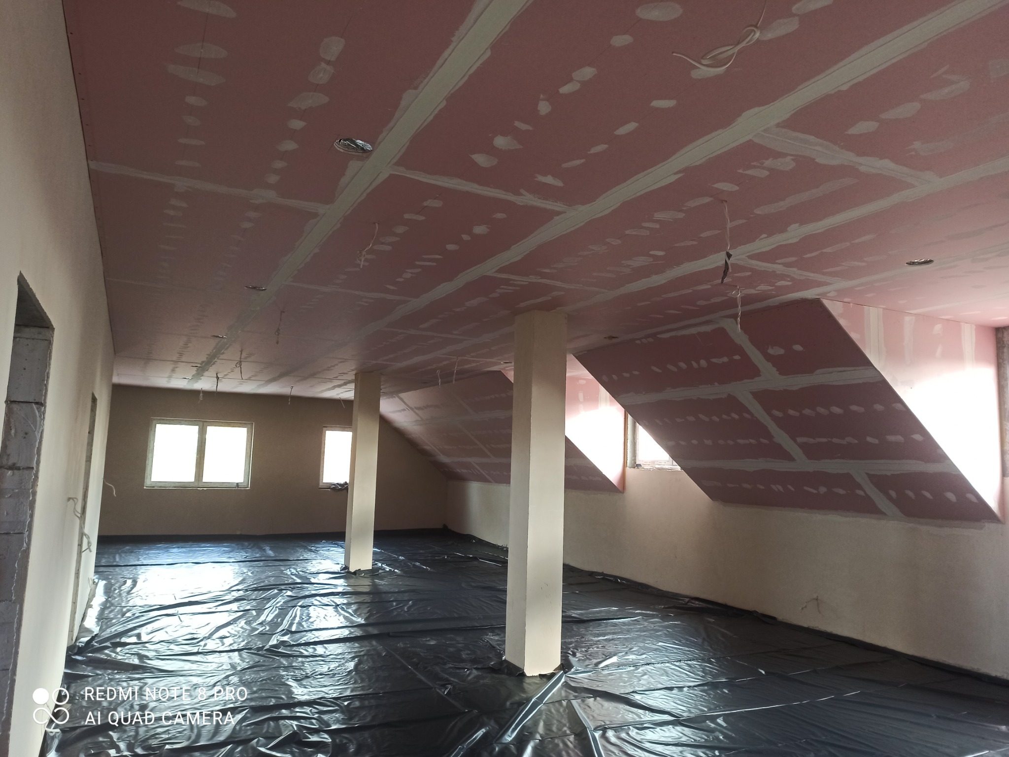 Montaż płyt karton gips na skośnym poddaszu, widoczne łączenia szpachlowane, podłoga zabezpieczona folią, instalacja elektryczna częściowo wyprowadzona.