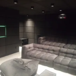 Wykończone, wyciszone kino domowe z szarą tapicerką ścian, modułowymi sofami, projektorem sufitowym i podświetleniem LED.