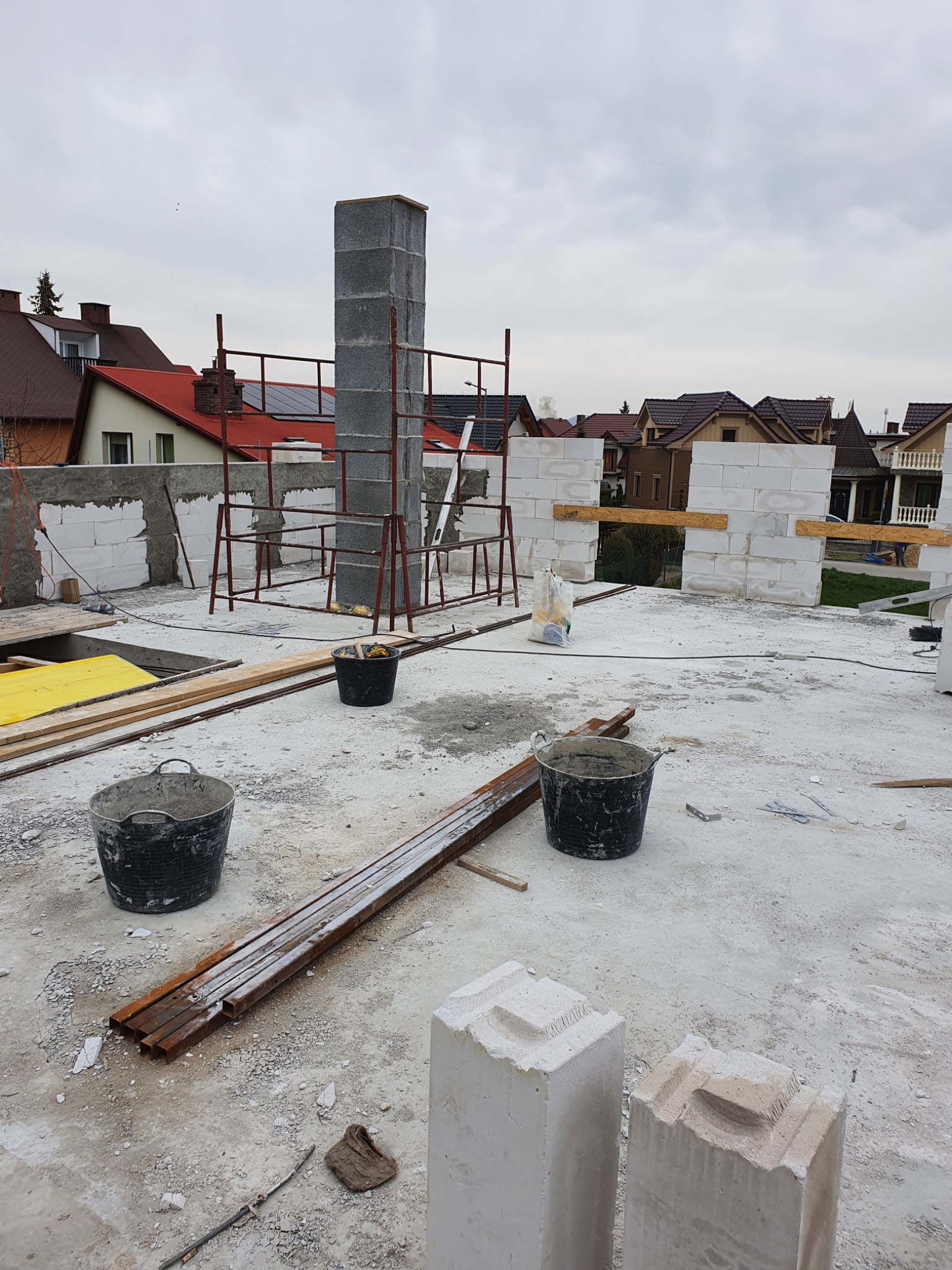 Budowa domu z betonu komórkowego: wznoszenie ścian i komina, widoczne rusztowania, narzędzia i materiały budowlane na dachu budynku w trakcie realizacji.