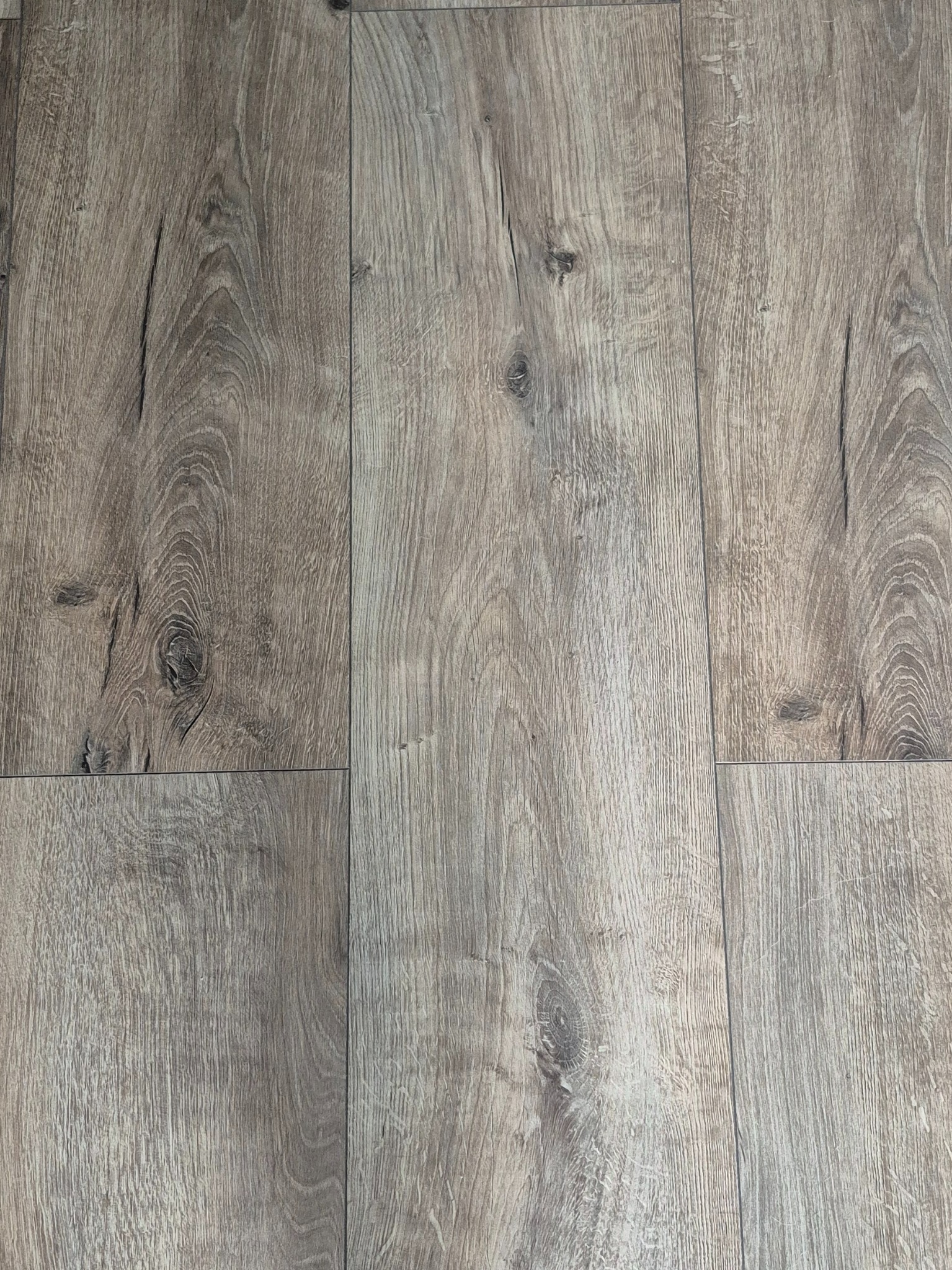 Jasne panele podłogowe z wyraźną strukturą drewna, ułożone w regularny wzór. Widoczne sęki i naturalne przebarwienia, podkreślające autentyczny wygląd podłogi.