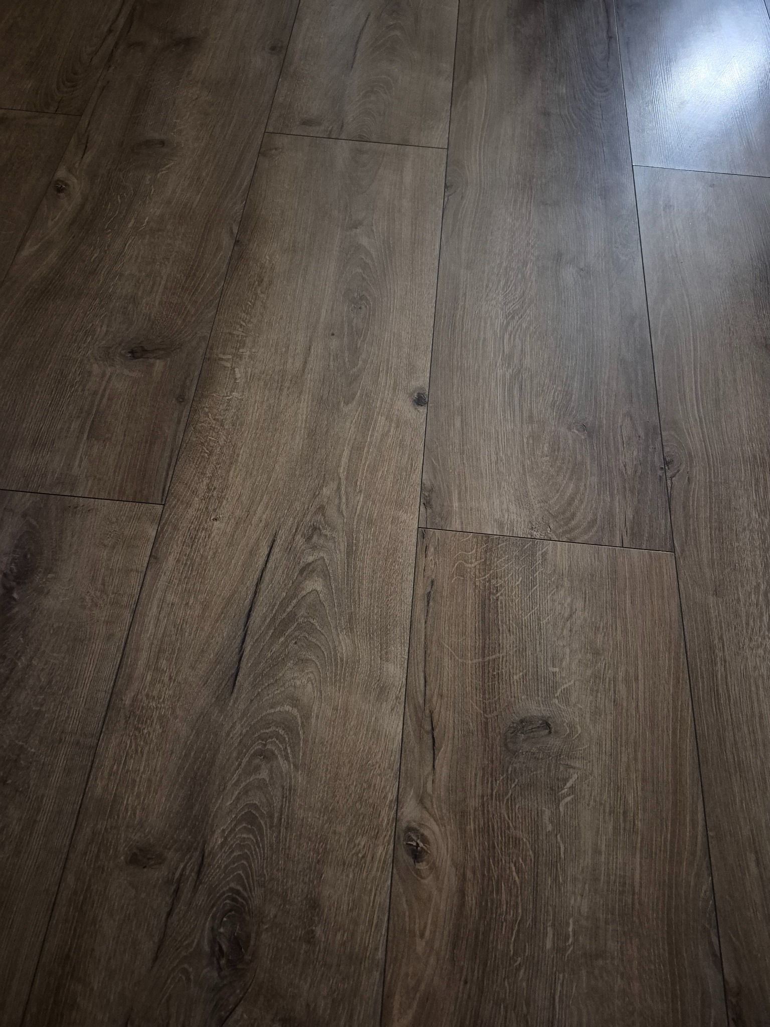 Ukończona podłoga z paneli w odcieniach brązu, imitująca naturalne drewno. Widoczne delikatne usłojenie i subtelne łączenia między panelami. Ujęcie pod kątem.