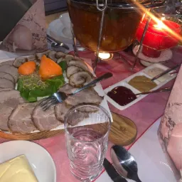 Dekoracyjnie podane dania mięsne z dodatkami, zupa w podgrzewaczu i sosy na stole z różową serwetą, świeca i nakrycie stołu.