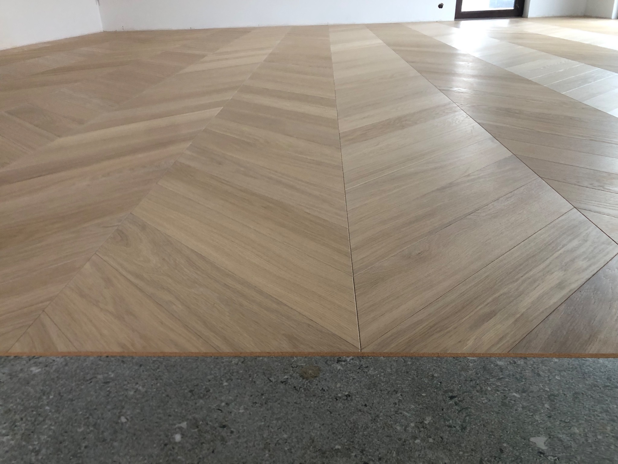 Ułożony parkiet w jodełkę francuską z widocznym surowym podłożem, jasne drewno, minimalistyczne wnętrze.