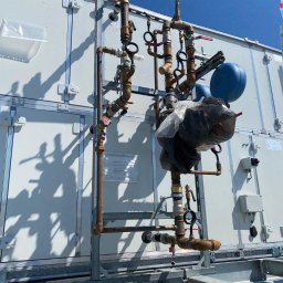 NOWY KLIMAT SPÓŁKA Z OGRANICZONĄ ODPOWIEDZIALNOŚCIĄ - Instalacja rur i zaworów, prawdopodobnie klimatyzacji, na dachu budynku we Wrocławiu, widoczne elementy konstrukcyjne i biała obudowa urządzenia.