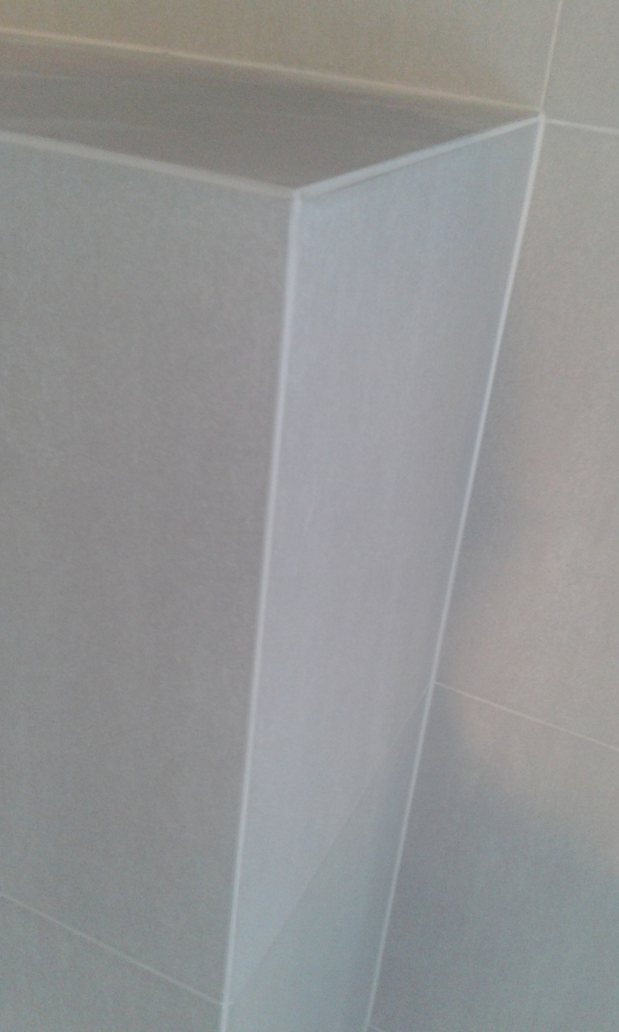 Szczegół narożnika wykończonego jasnoszarymi płytkami ceramicznymi, widoczne fugi i precyzyjne cięcia płytek.