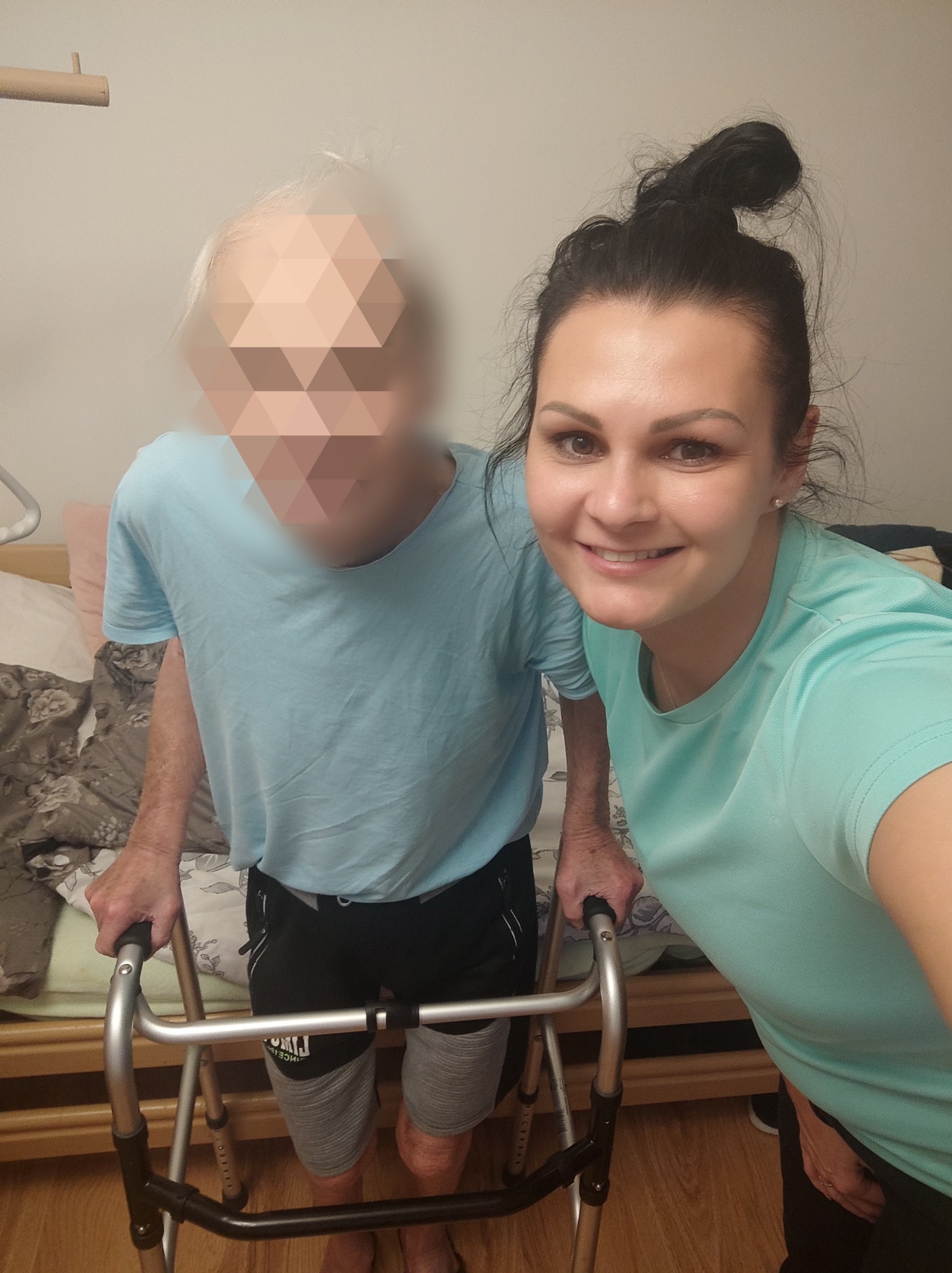 Opiekunka pozuje do zdjęcia z seniorem korzystającym z chodzika w Kędzierzynie-Koźlu. Obie osoby ubrane w błękitne koszulki.