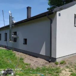 Elewacja budynku jednorodzinnego po ociepleniu, z widocznym kominem ceramicznym i stalowym systemem odprowadzania spalin, antena telewizyjna na dachu.
