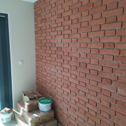 GENERAL-BUD Piotr Porczyński - Ściana z cegieł dekoracyjnych w Dobroniu Małym, z widocznymi materiałami budowlanymi w kartonach i wiaderkach, czekająca na dalsze prace wykończeniowe.