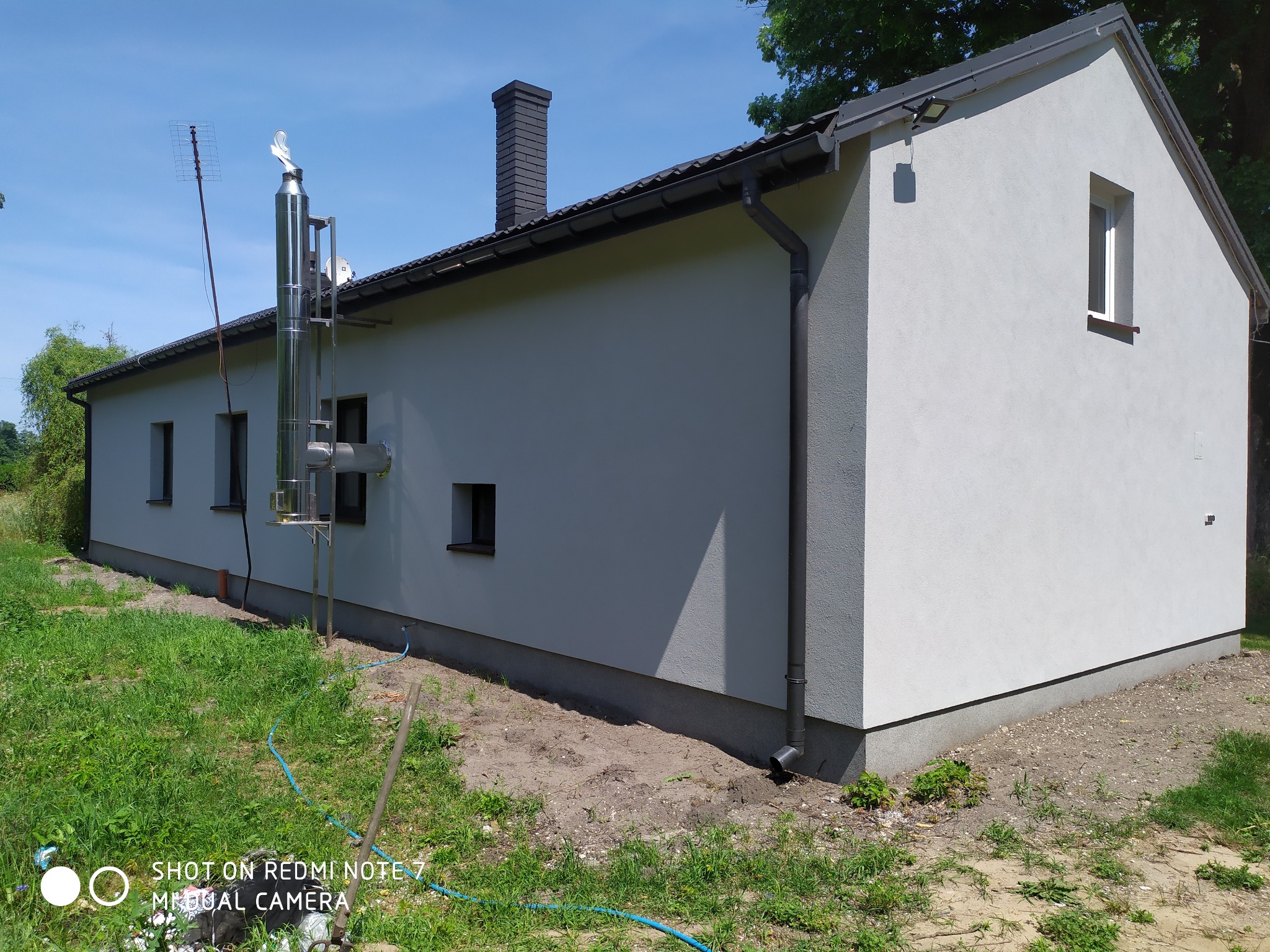 Elewacja budynku jednorodzinnego po ociepleniu, z widocznym kominem ceramicznym i stalowym systemem odprowadzania spalin, antena telewizyjna na dachu.