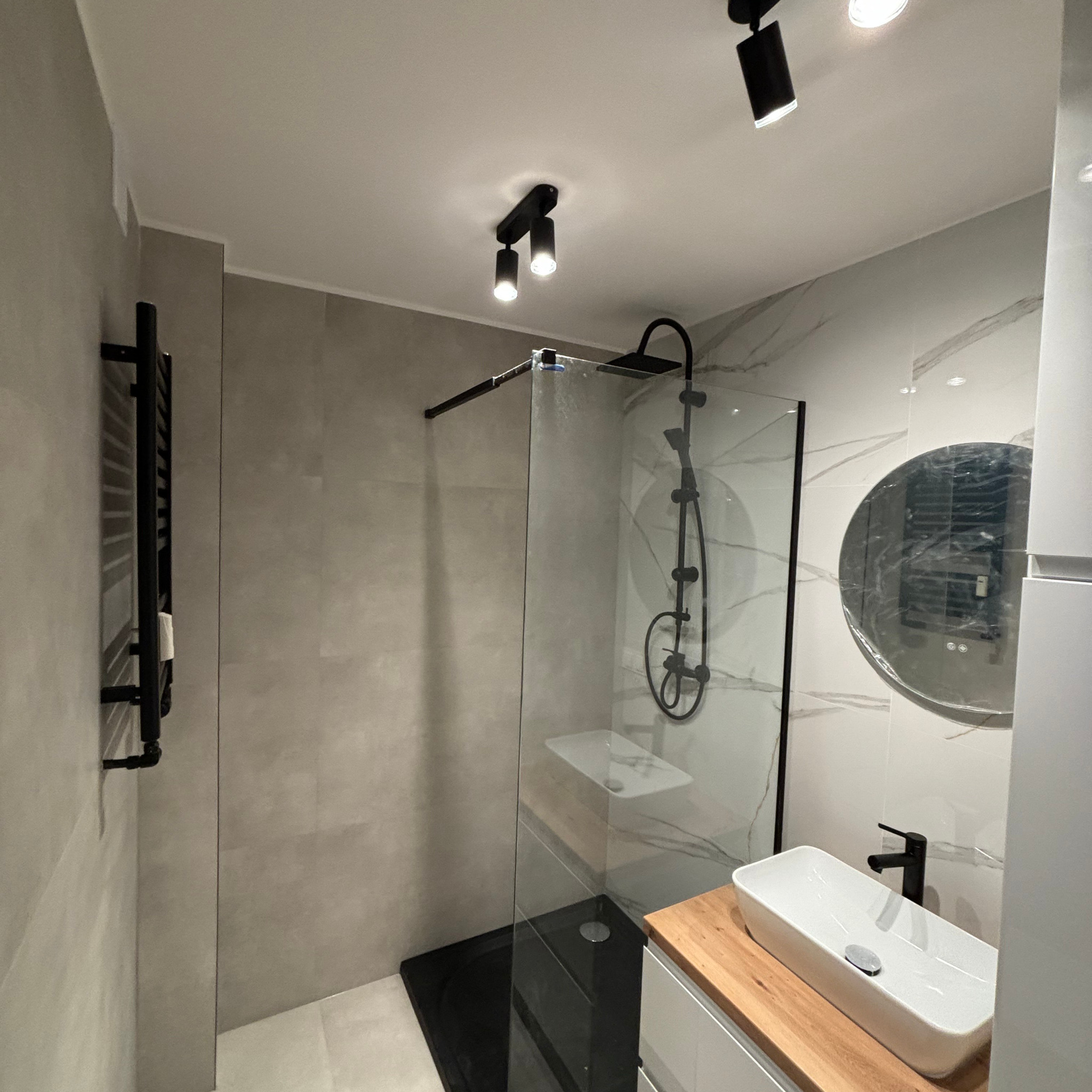 Nowoczesna łazienka z kabiną prysznicową typu walk-in z czarnym brodzikiem, grzejnikiem drabinkowym i umywalką nablatową na drewnianym blacie.