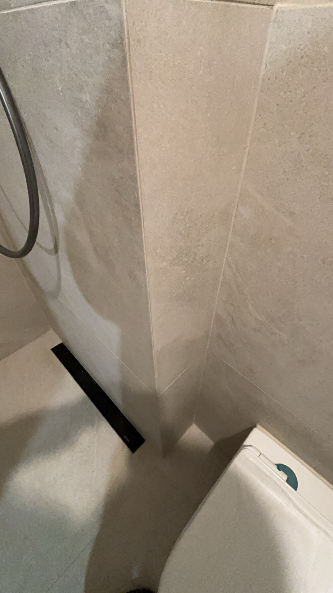 Neutralne, beżowe płytki na ścianie i podłodze w łazience, z widocznym odpływem liniowym i fragmentem wanny.