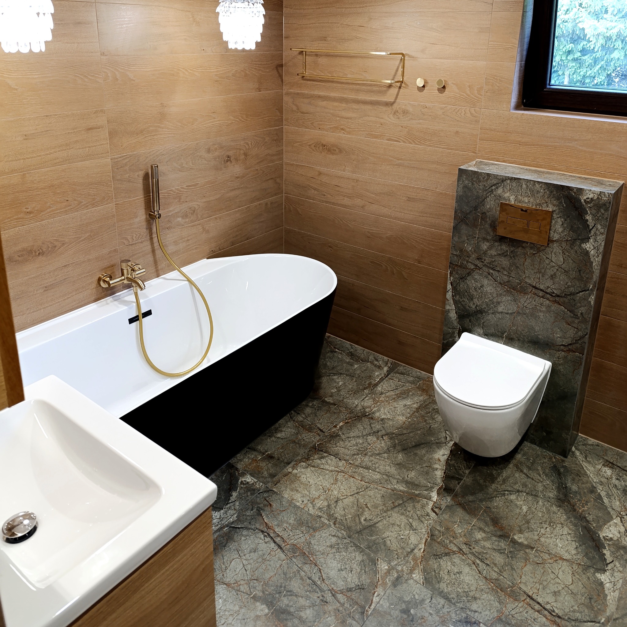 Nowoczesna łazienka z drewnopodobnymi płytkami ściennymi, czarną wanną i marmurową podłogą. Złota armatura i oświetlenie dodają elegancji.