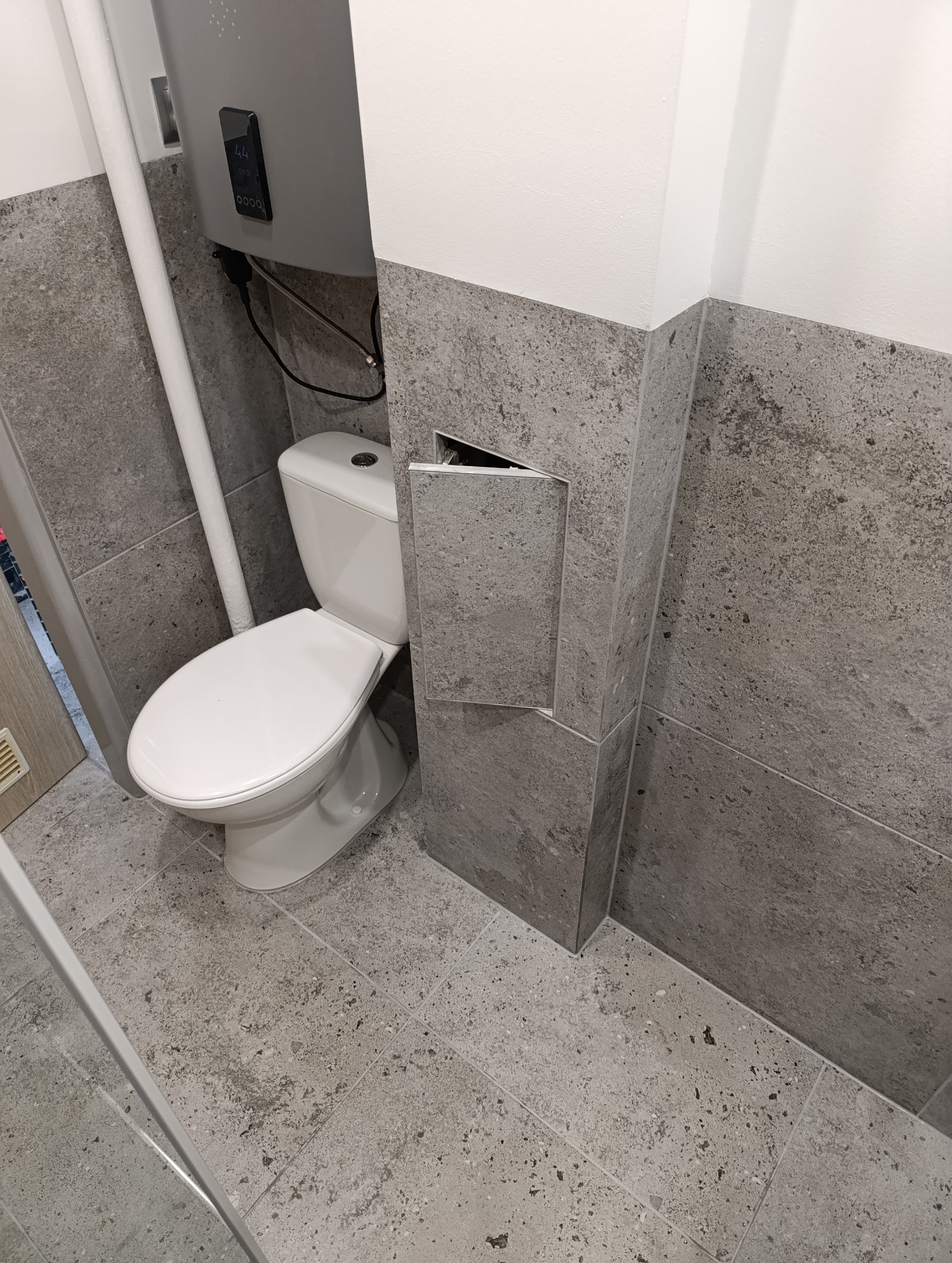 Wykończona łazienka z toaletą i ukrytą spłuczką w szarej, kamiennej okładzinie. Minimalistyczny design, nowoczesne wykończenie.