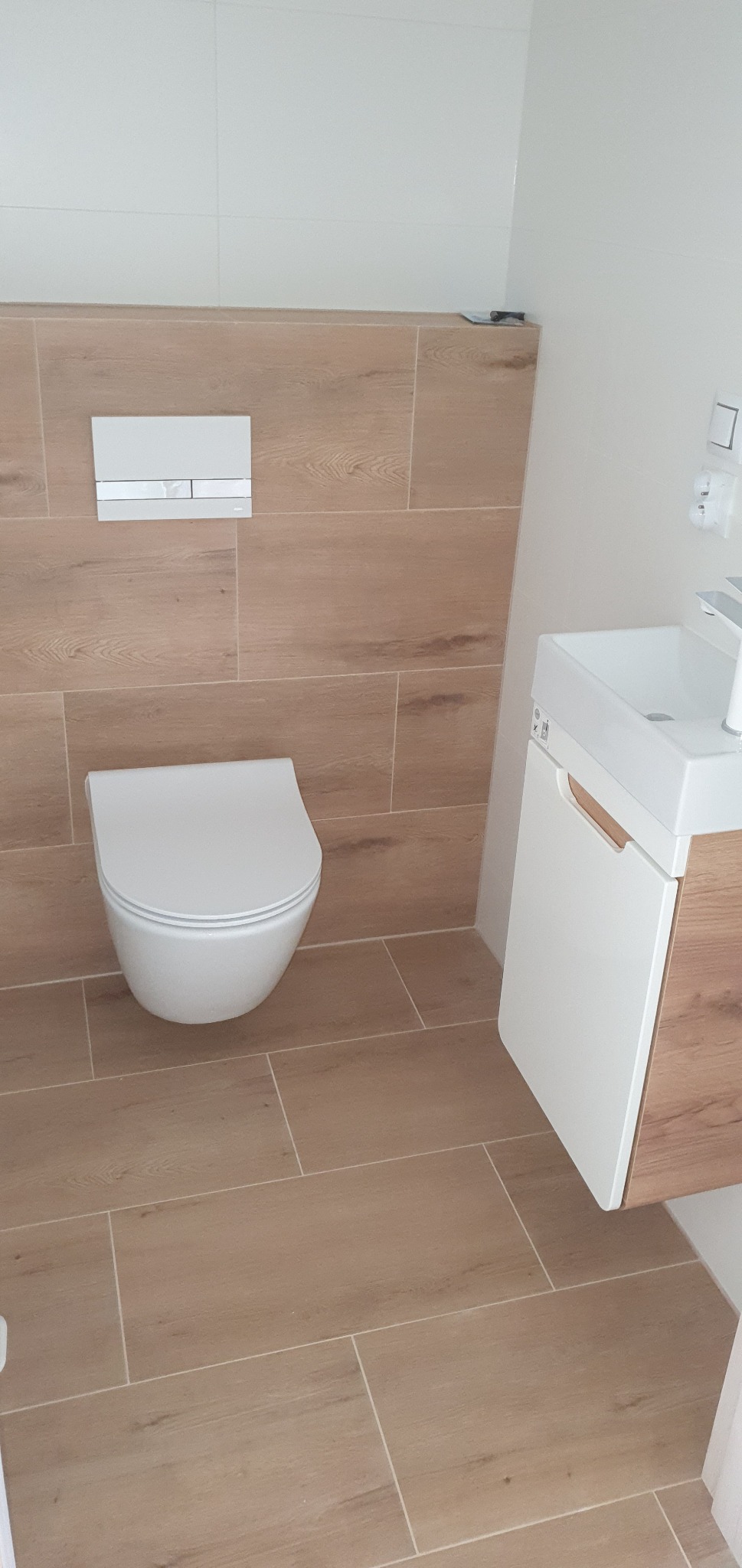 Nowoczesna łazienka z podwieszaną toaletą, umywalką z szafką z drewnianymi akcentami i płytkami imitującymi drewno na podłodze i ścianie.