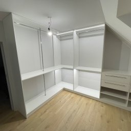 SZWAGRY DESIGN meble z pasją - Biała garderoba z półkami i drążkami na ubrania, wkomponowana w skos dachu, oświetlona listwą LED, z drewnianą podłogą