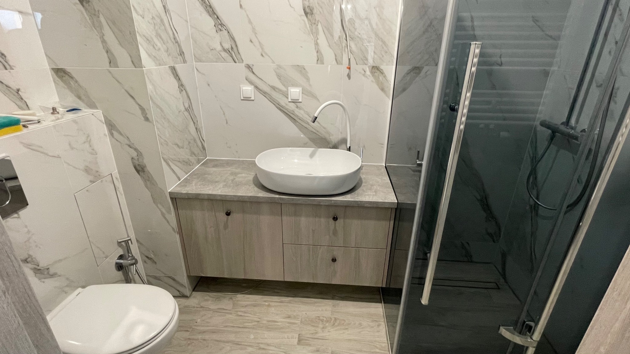 Nowoczesna łazienka z umywalką nablatową na szafce z szufladami, kabina prysznicowa w tle, marmurowe płytki na ścianach i podłodze.