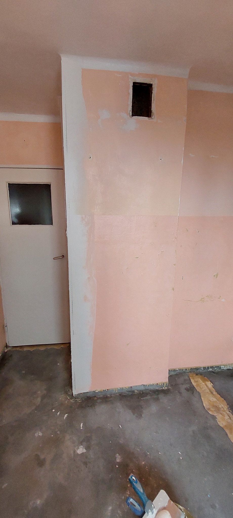 Ściana w trakcie przygotowania do malowania w Strzyżowie, z widocznymi śladami szpachlowania i otworem wentylacyjnym, podłoga zabezpieczona folią malarską.