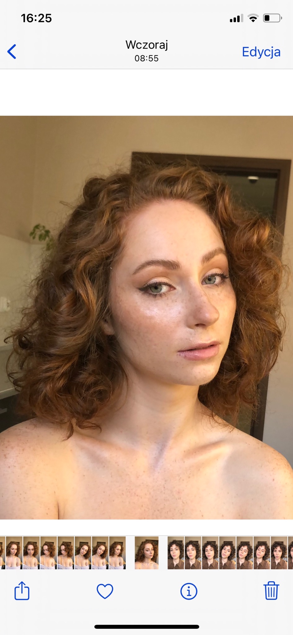 Portret kobiety z rudymi kręconymi włosami i delikatnym, rozświetlającym makijażem, podkreślającym oczy eyelinerem i beżowymi cieniami, widoczne piegi na twarzy i dekolcie.