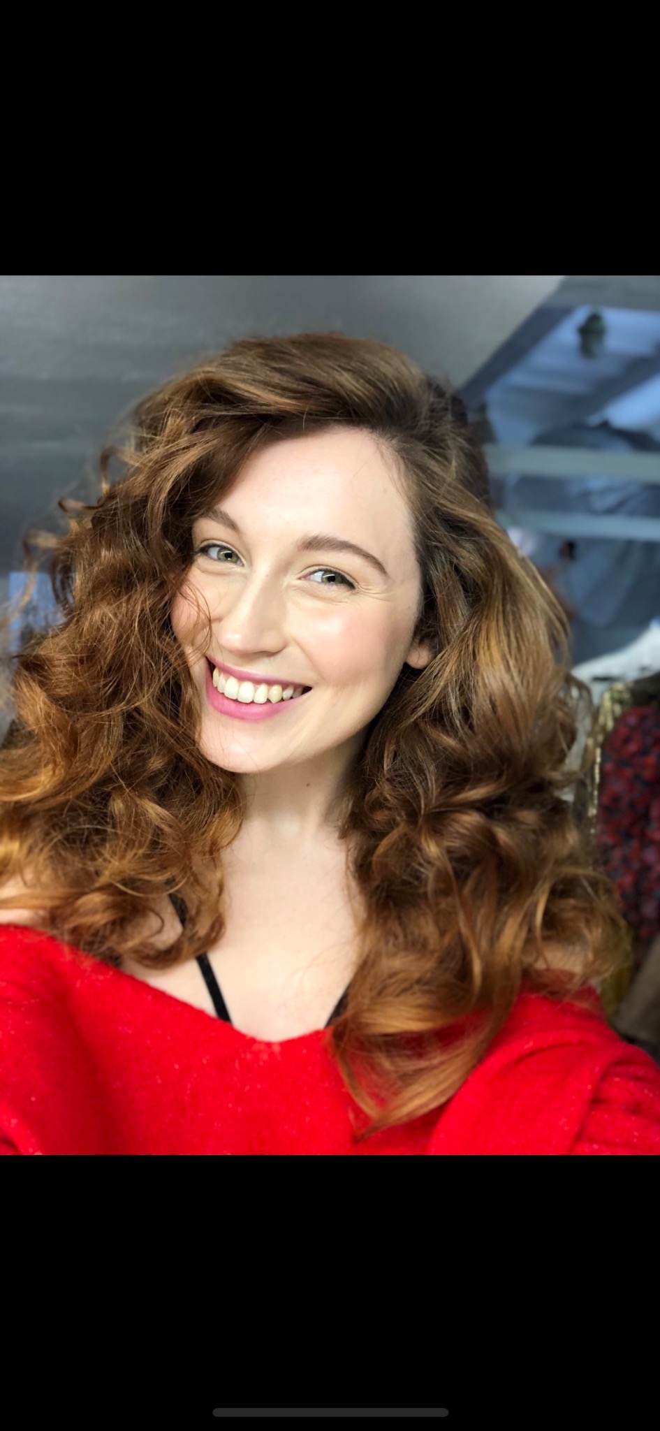 Uśmiechnięta kobieta z rudymi, kręconymi włosami i delikatnym, naturalnym podkreśleniem policzków, prezentująca efekt zabiegu kosmetycznego.