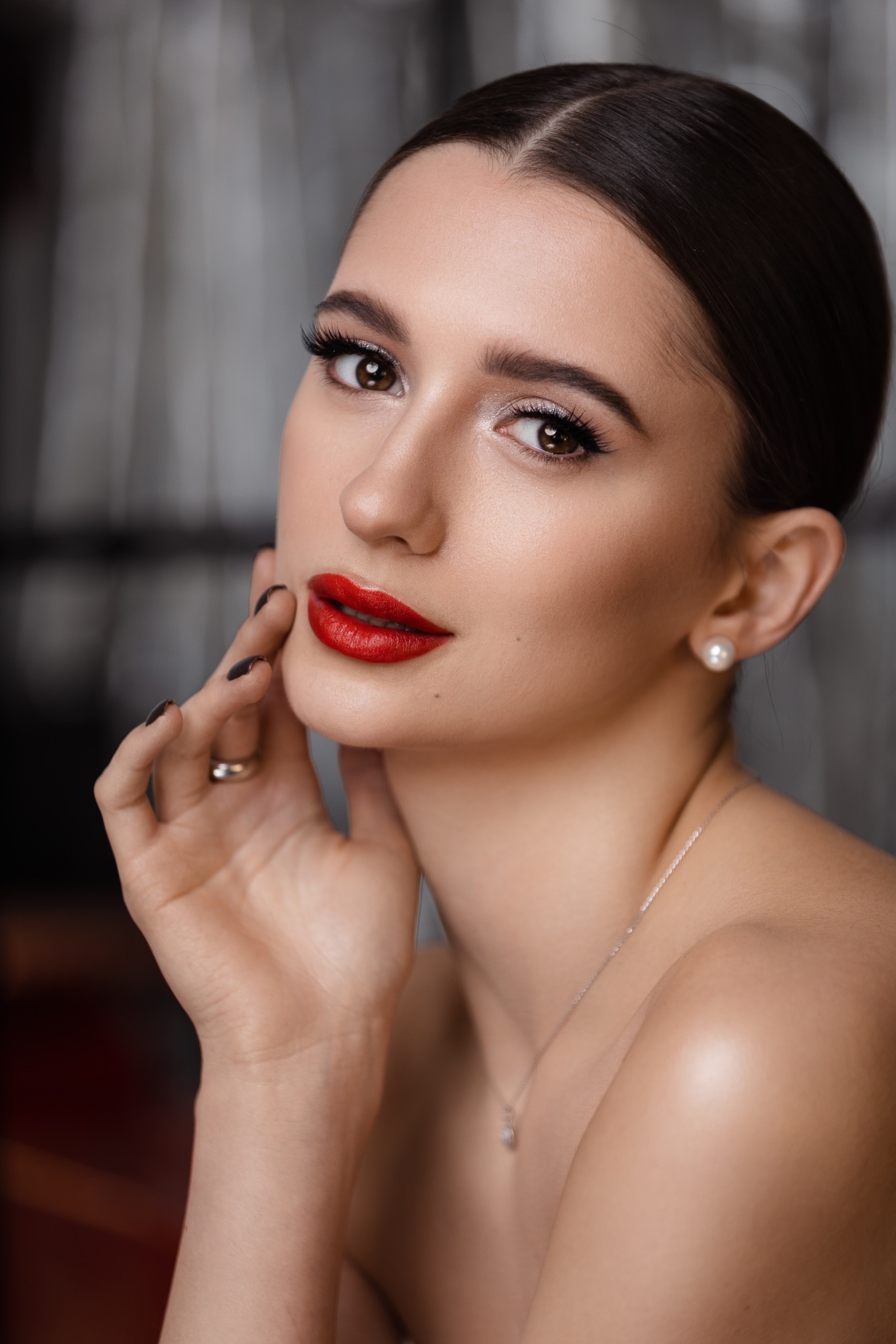 Portret kobiety z profesjonalnym makijażem: intensywna czerwona szminka, podkreślone oczy z długimi rzęsami, delikatny kontur twarzy, elegancka fryzura z gładko zaczesanymi włosami, perłowe...