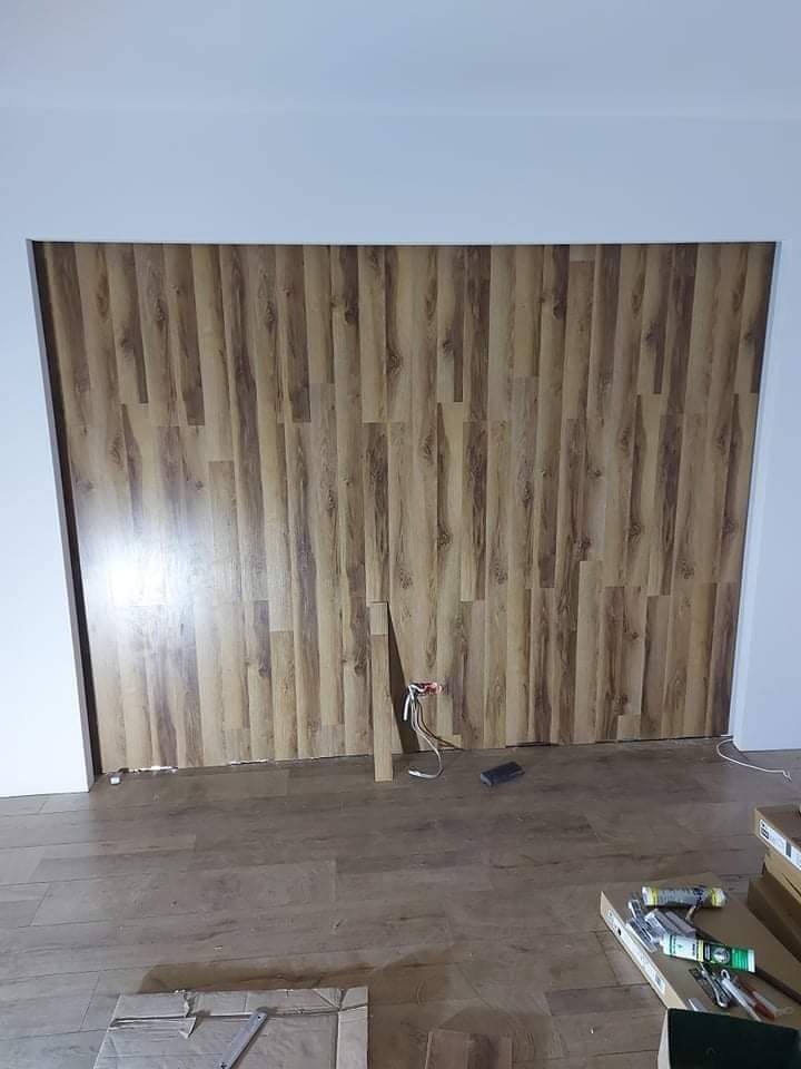 Ściana wyłożona panelami imitującymi drewno w trakcie montażu, widoczne przewody elektryczne i narzędzia na podłodze.