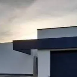 Nowoczesny budynek jednorodzinny z elewacją w kolorze białym i grafitowym, widok z boku, lekko pochmurne niebo w tle.