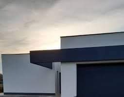 Nowoczesny budynek jednorodzinny z elewacją w kolorze białym i grafitowym, widok z boku, lekko pochmurne niebo w tle.