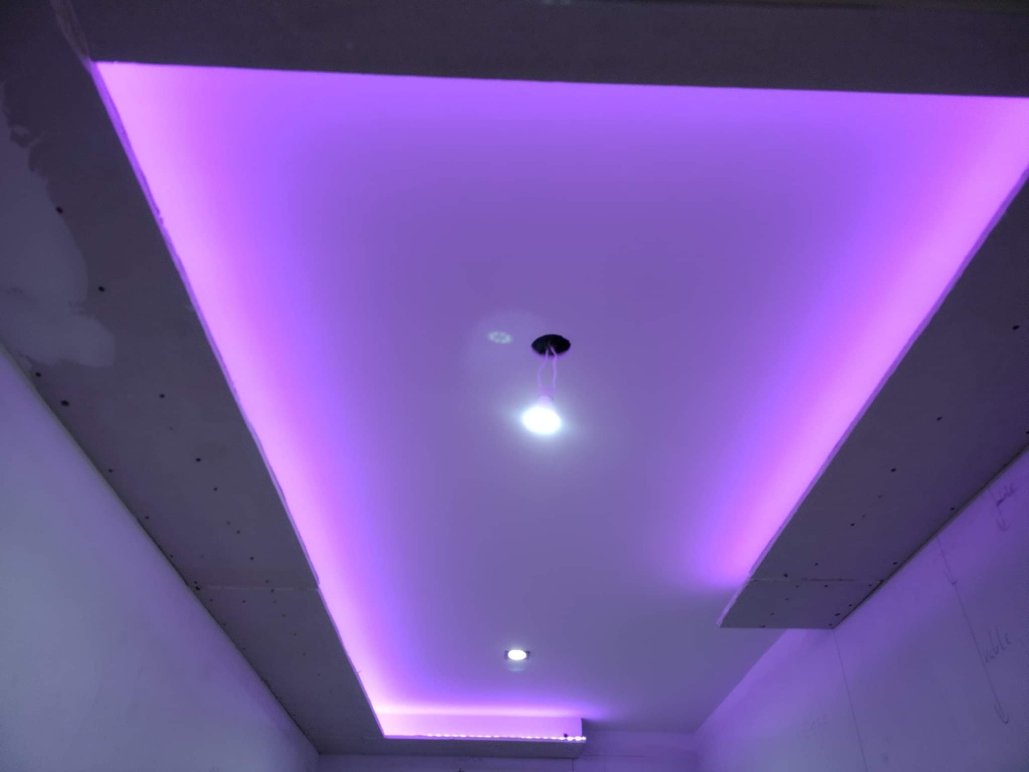 Sufit podwieszany z oświetleniem LED w odcieniach fioletu, widoczne niedoskonałości na powierzchni płyt gipsowo-kartonowych przed wykończeniem.